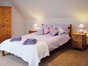 A bedroom with a bed, two nightstands, a wooden wardrobe, and a carpeted floor.