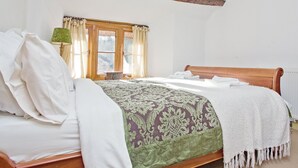 A bedroom with a wooden bed, a window with curtains, and a lamp. - 4 bedroom accommodation in Dulverton (Dulverton)