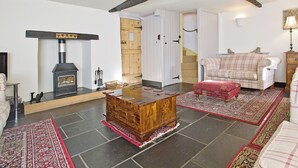 A cozy living room with a fireplace, a wooden chest of drawers, a plaid sofa, and a staircase leading to another room. - 4 bedroom accommodation in Dulverton (Dulverton)