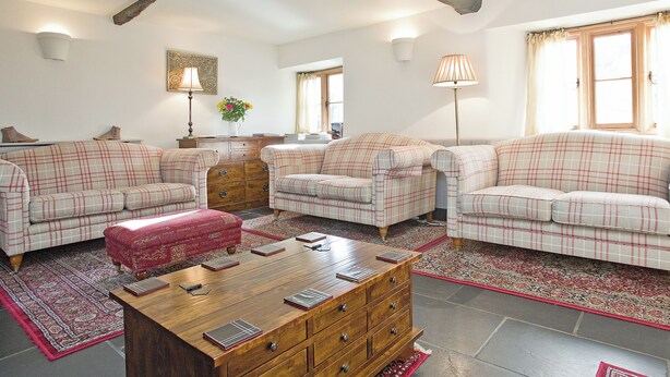 A living room with a wooden coffee table, two plaid sofas, a red ottoman, and a patterned rug. - 4 bedroom accommodation in Dulverton (Dulverton)