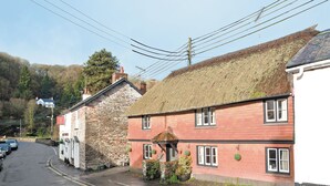 A traditional stone and brick building with a thatched roof, a stone chimney, and a small garden area with potted plants. - 4 bedroom accommodation in Dulverton (Dulverton)