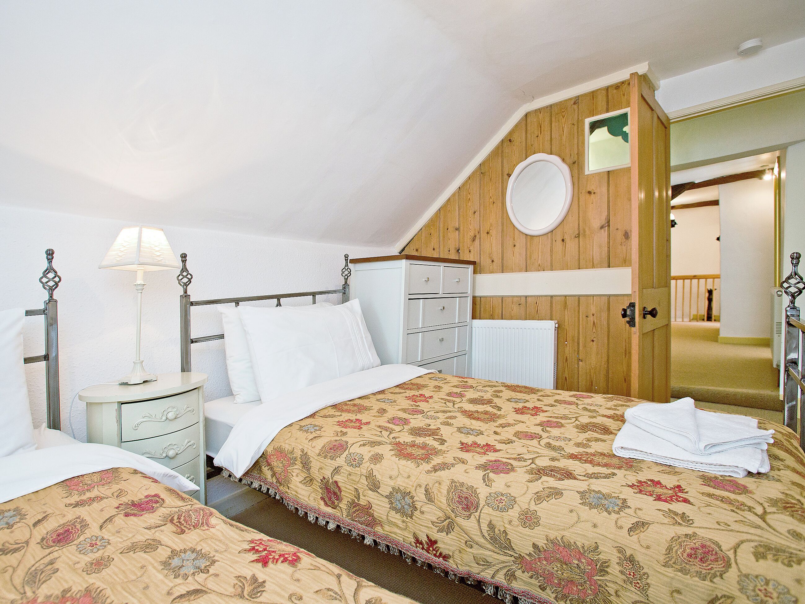 A bedroom with two beds, a nightstand, a dresser, and a wooden wall with a mirror.