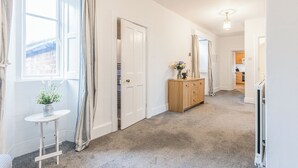 A hallway with a carpeted floor, a white door, a wooden dresser with a vase of flowers, and a small table with a plant. - 2 bedroom accommodation in Old Hunstanton (Old Hunstanton)