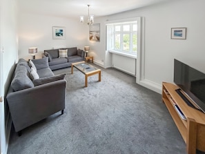 A modern living room with a grey sofa set, a coffee table, a TV stand, and a large window with a view. - 2 bedroom accommodation in Old Hunstanton (Old Hunstanton)
