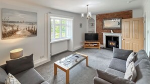 A living room with a sofa set, a coffee table, a TV, a fireplace, and a painting on the wall. - 2 bedroom accommodation in Old Hunstanton (Old Hunstanton)