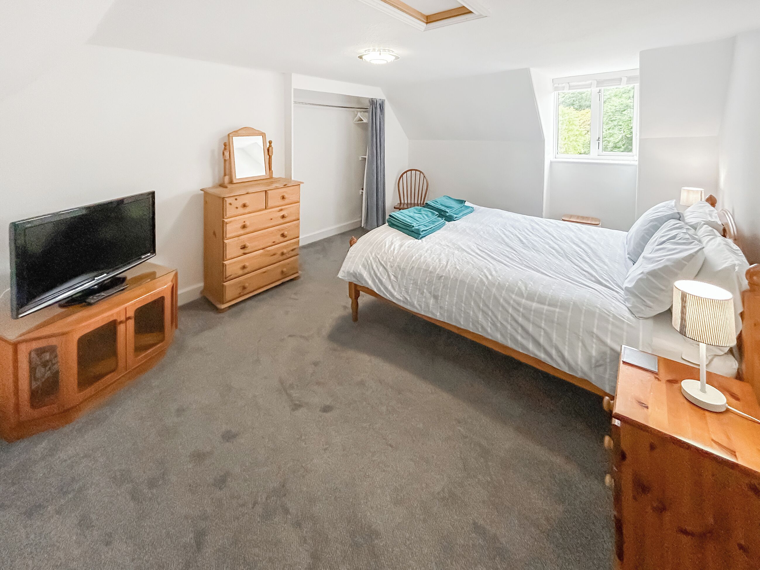 Een slaapkamer met een bed, een televisie op een houten dressoir, een kast en een raam.