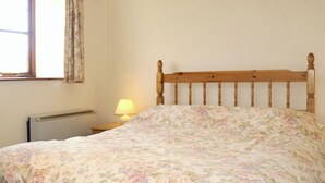 Une chambre à coucher avec une tête de lit en bois, une couvre-lit à motifs floraux, une lampe de chevet et un radiateur.