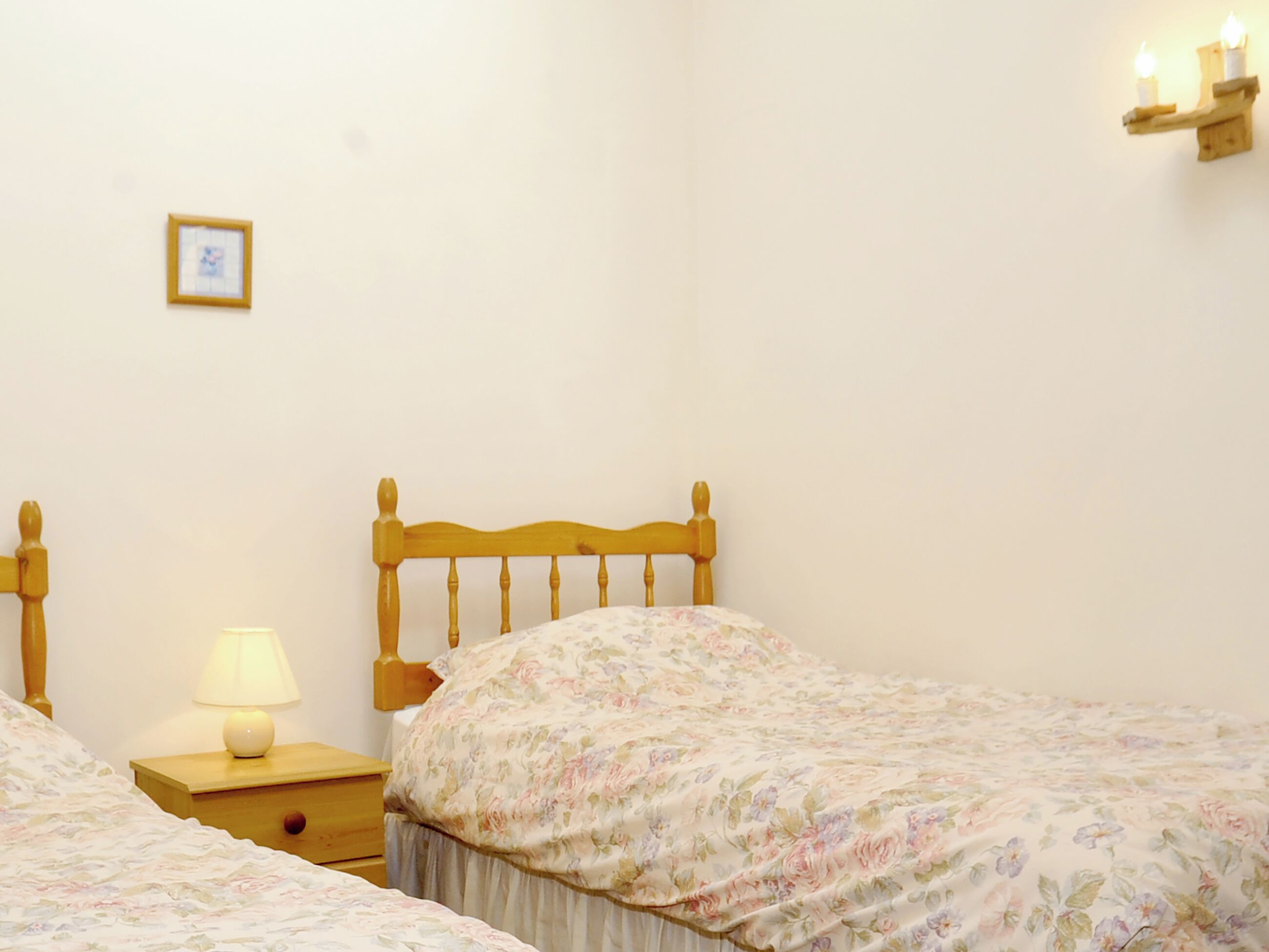 Un dormitorio con dos camas individuales, una mesita de noche con lámpara, un cuadro en la pared e iluminación en la pared.