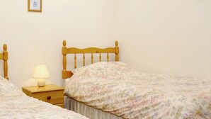 Un dormitorio con dos camas individuales, una mesita de noche con lámpara, un cuadro en la pared e iluminación en la pared.