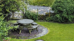 A wooden table and benches in a garden with a stone pathway, surrounded by lush greenery and a view of a river. - 3 bedroom accommodation in Oughtershaw, near Hawes (Oughtershaw, near Hawes)
