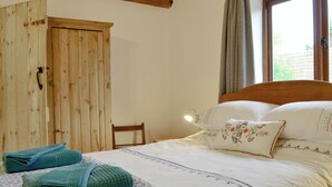 A bedroom with a bed, a wooden wardrobe, and a window with curtains. - The Wood Shed - E1919 (Hinton, near Dunwich)