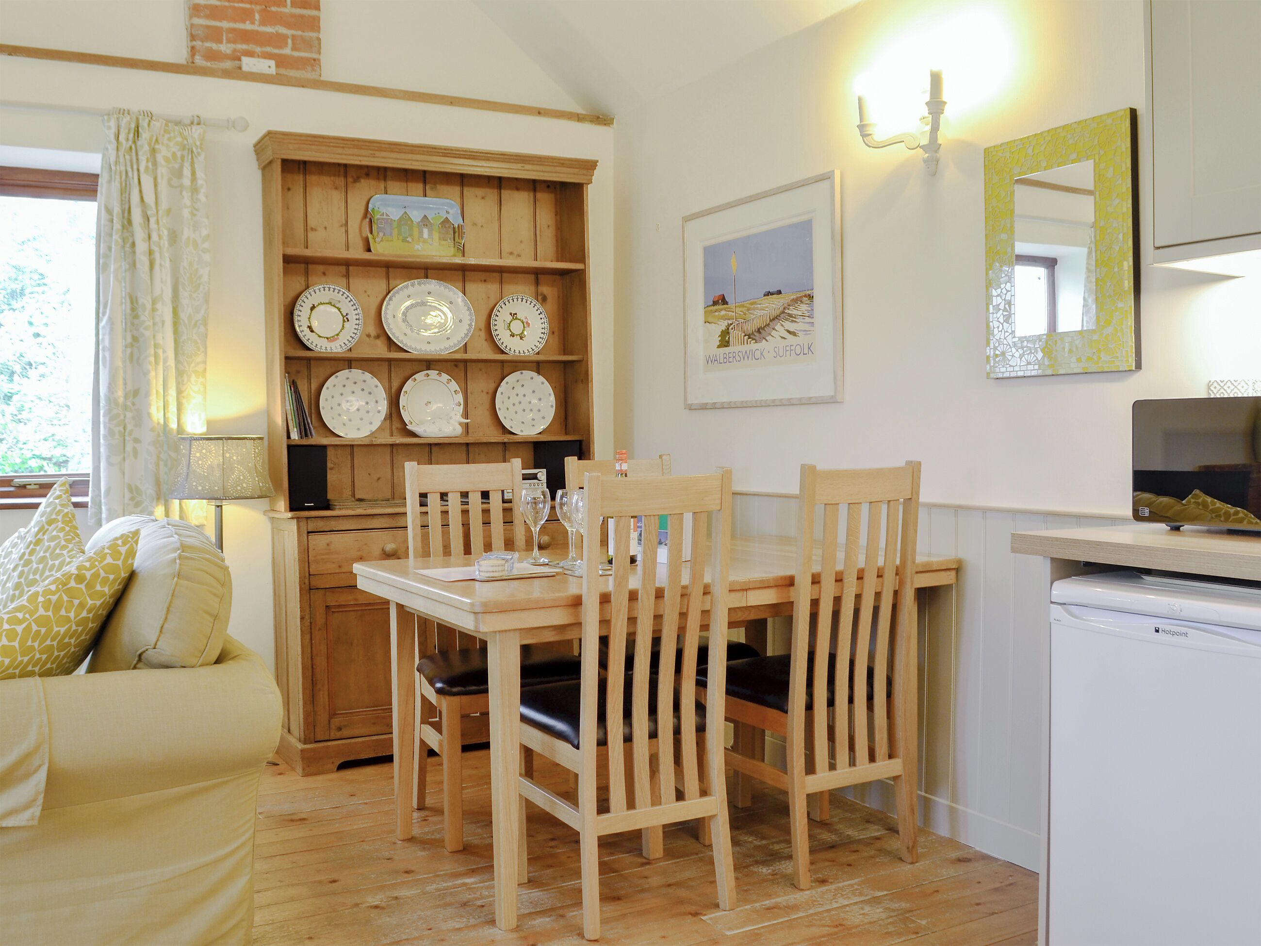 A cozy dining area with wooden furniture, a shelf with decorative plates, and a framed landscape painting.
