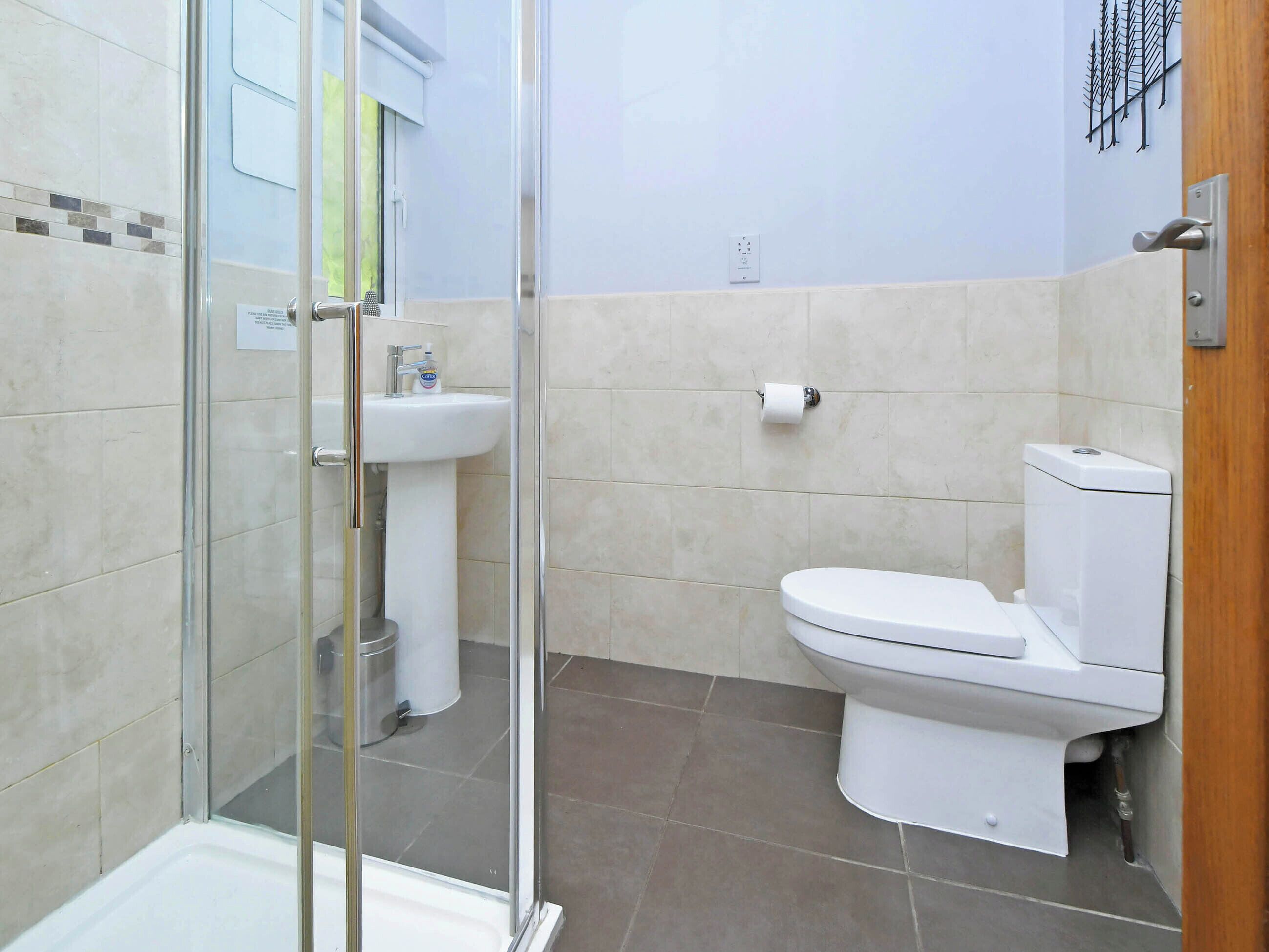 A bathroom with a glass shower enclosure, a pedestal sink, and a toilet.