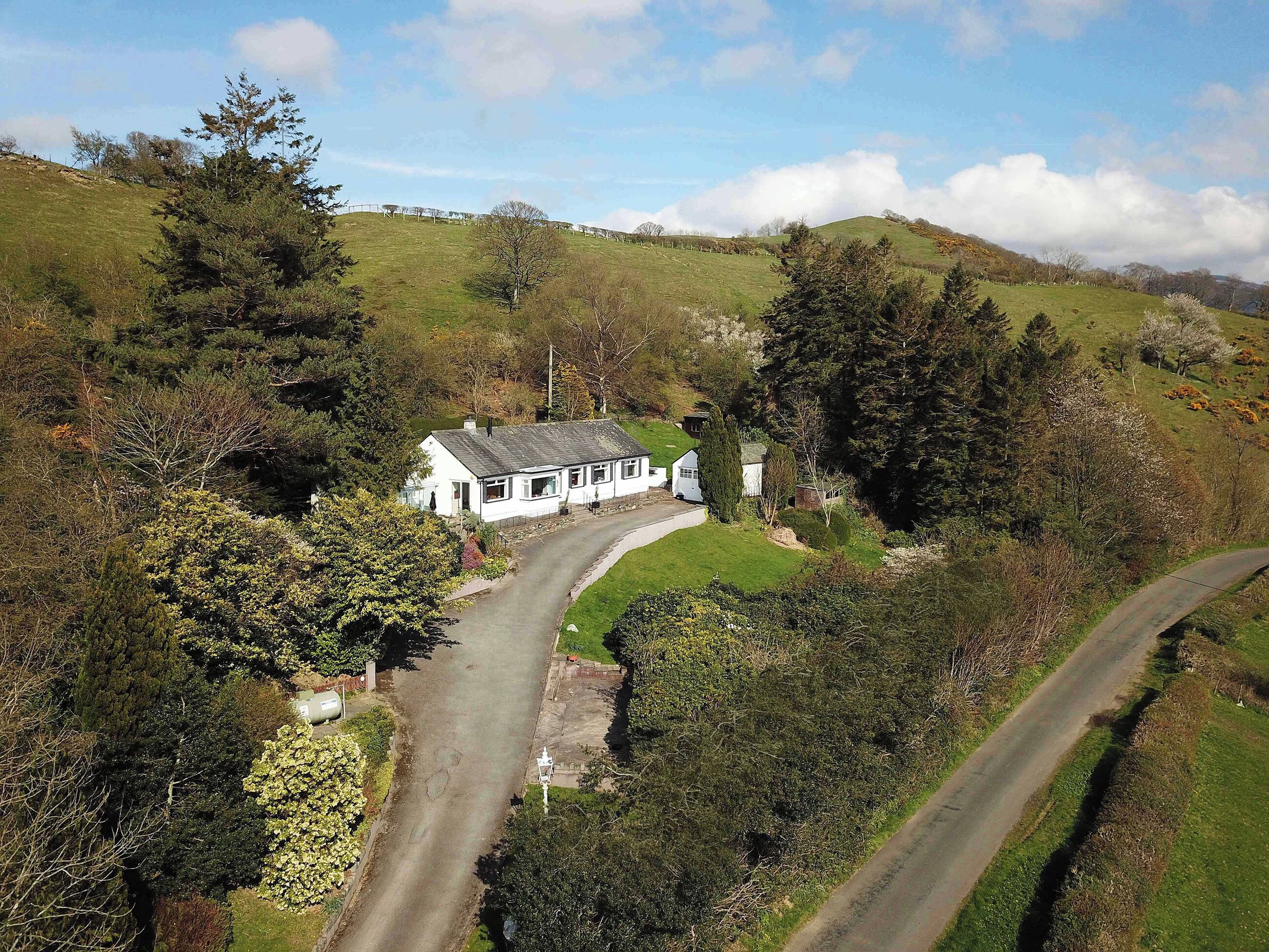 A white house with a sloped roof, surrounded by greenery and a winding road.