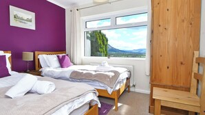 A bedroom with two beds, a wooden wardrobe, a window with a view of mountains, and a painting on the wall. - 4 bedroom accommodation in Bassenthwaite, near Keswick (Bassenthwaite, near Keswick)