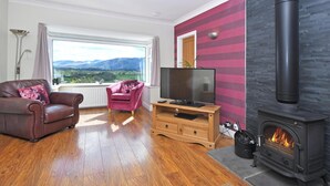 A living room with a fireplace, a television, a sofa, and a view of the outdoors. - 4 bedroom accommodation in Bassenthwaite, near Keswick (Bassenthwaite, near Keswick)