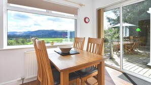 A dining area with a table and chairs, a view of the outdoors, a radiator, and a clock on the wall. - 4 bedroom accommodation in Bassenthwaite, near Keswick (Bassenthwaite, near Keswick)
