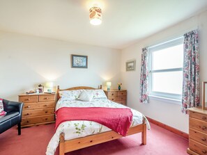 A bedroom with a wooden bed, a nightstand, a dresser, a chair, and a window with curtains.