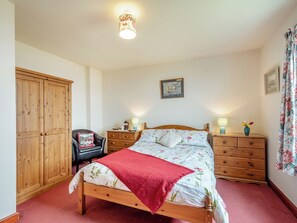 A bedroom with a wooden bed, a wardrobe, a chair, a nightstand, and a lamp. - Spacious family cottage with open fire and garden overlooking the sea. (Drummore, near Stranraer)