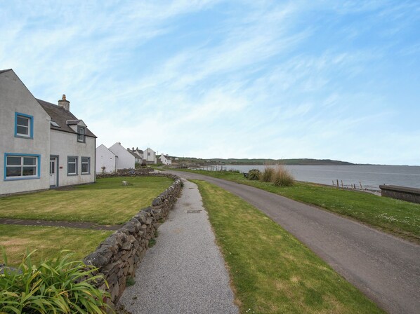 A coastal road with stone walls and a grassy path leading to houses with blue trim.