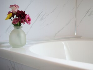 A bathroom with a marble wall and a white bathtub.
