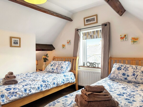 A bedroom with two single beds, a window with curtains, a radiator, and a framed picture on the wall.