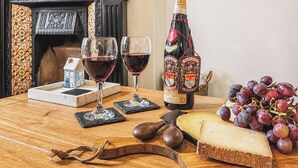 A wooden table with a bottle of wine, two glasses of red wine, a piece of cheese, and a bunch of grapes. - 2 bedroom accommodation in Keswick (Keswick)