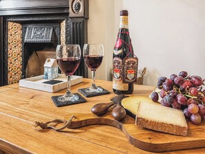 Une table en bois, une bouteille de vin, deux verres de vin rouge, un morceau de fromage et une grappe de raisins.