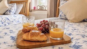 A bed with floral bedding, a wooden tray with croissants and fruit, and a glass of orange juice. - 2 bedroom accommodation in Keswick (Keswick)