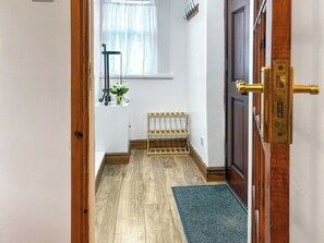 Un pasillo con un banco de madera, un estante pequeño con flores y una puerta con picaporte de latón.
