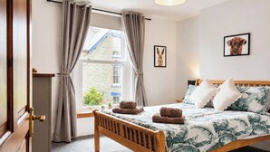 A bedroom with a wooden bed, grey curtains, a window with a view of a building, and a framed picture on the wall. - 2 bedroom accommodation in Keswick (Keswick)