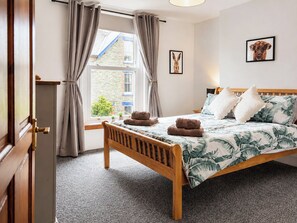 Une chambre à coucher avec un lit en bois, une fenêtre avec des rideaux, une petite table de chevet et un tableau accroché au mur.