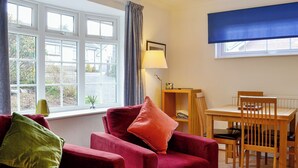 Ein Zimmer mit einem roten Sofa, einem Holzesstisch und einem Fenster mit Vorhängen.