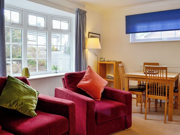 A room with a red sofa, a wooden dining table, and a window with curtains. - 2 bedroom accommodation in Keswick (Keswick)