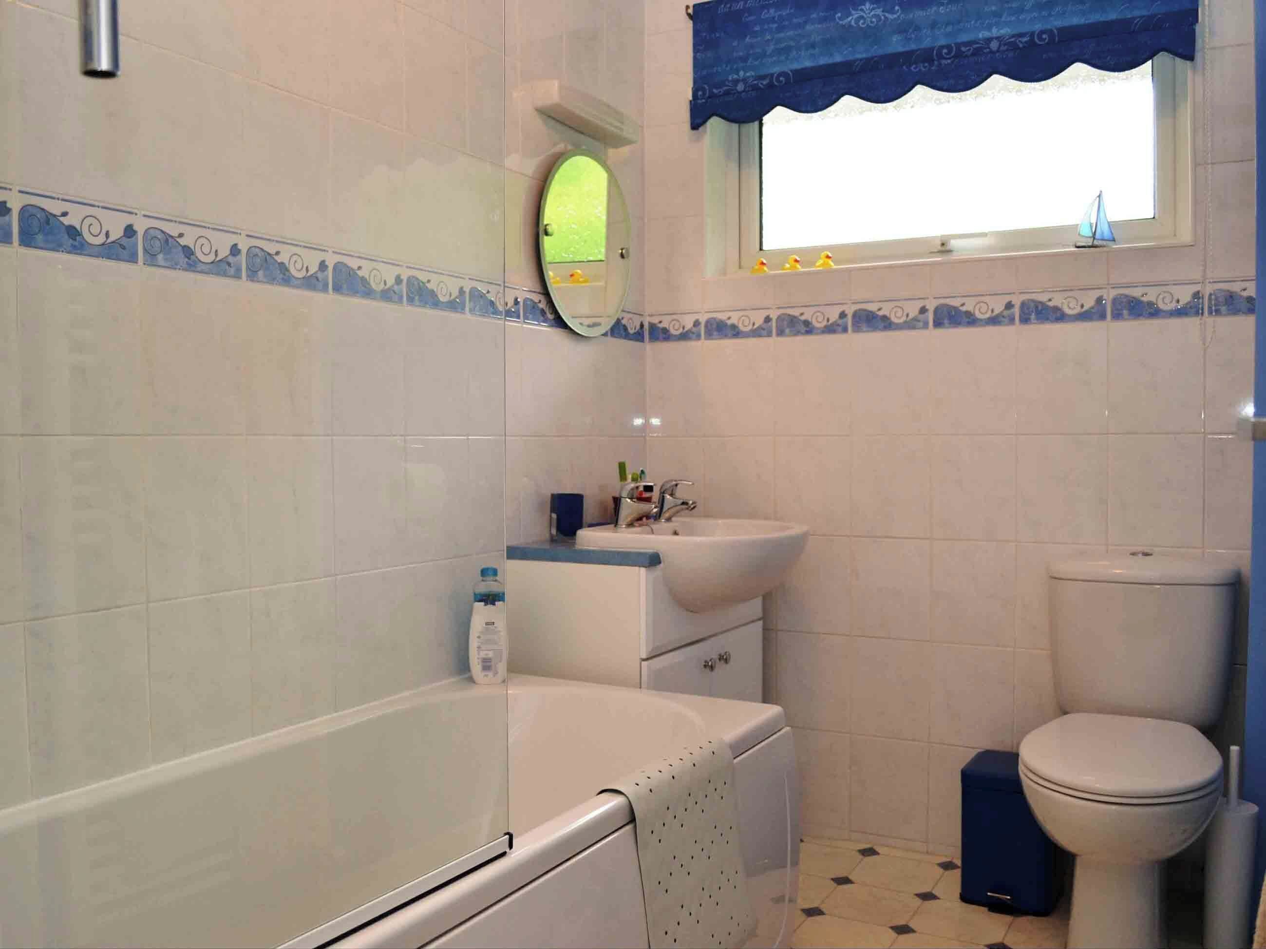 A bathroom with a bathtub, sink, toilet, and a window with a blue curtain.