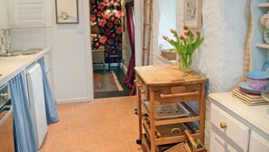 A kitchen with a tiled floor, a wooden table with a vase of tulips, and a white cabinet with dishes.
