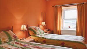 Un dormitorio con dos camas, una mesita de noche, una lámpara y una ventana con cortinas.