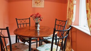 Una mesa de comedor con sillas, un florero, un cuadro en la pared y un ventanal con cortinas.