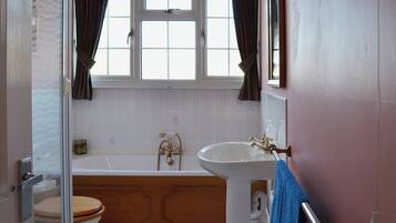 A bathroom with a white bathtub, a white sink, and a wooden toilet.