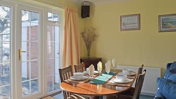 A dining area with a wooden table set for four, a vase with dried plants, and two framed pictures on the wall.
