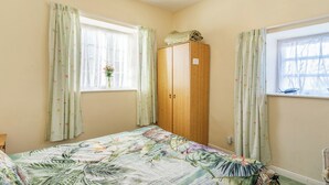Ein Schlafzimmer mit einem Bett, zwei mit Vorhängen versehenen Fenstern, einem Holzschrank und einer Deckenleuchte.