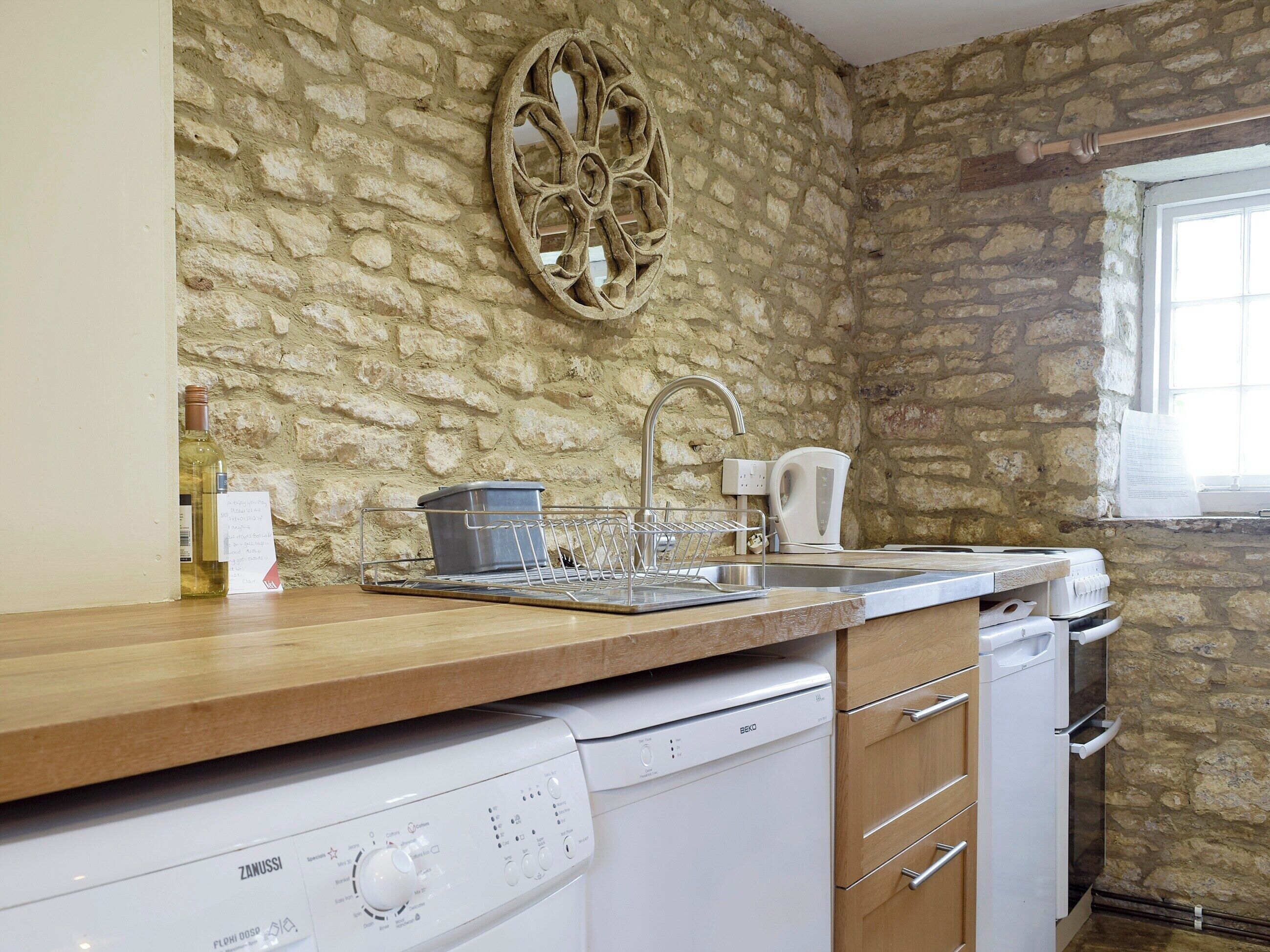 Una cocina con pared de piedra, encimera de madera, lavavajillas y cafetera.