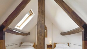 Un dormitorio con dos camas individuales, vigas de madera, un tragaluz y una mesita de noche pequeña con lámpara.