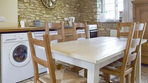 Una cocina con pared de piedra, lavadora, estufa y sillas de madera alrededor de una mesa.