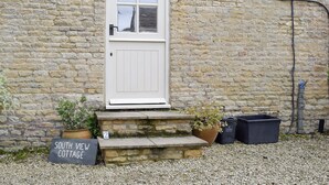 Una cabaña de piedra con una puerta blanca, escalones y un cartel que dice 'South View Cottage'.