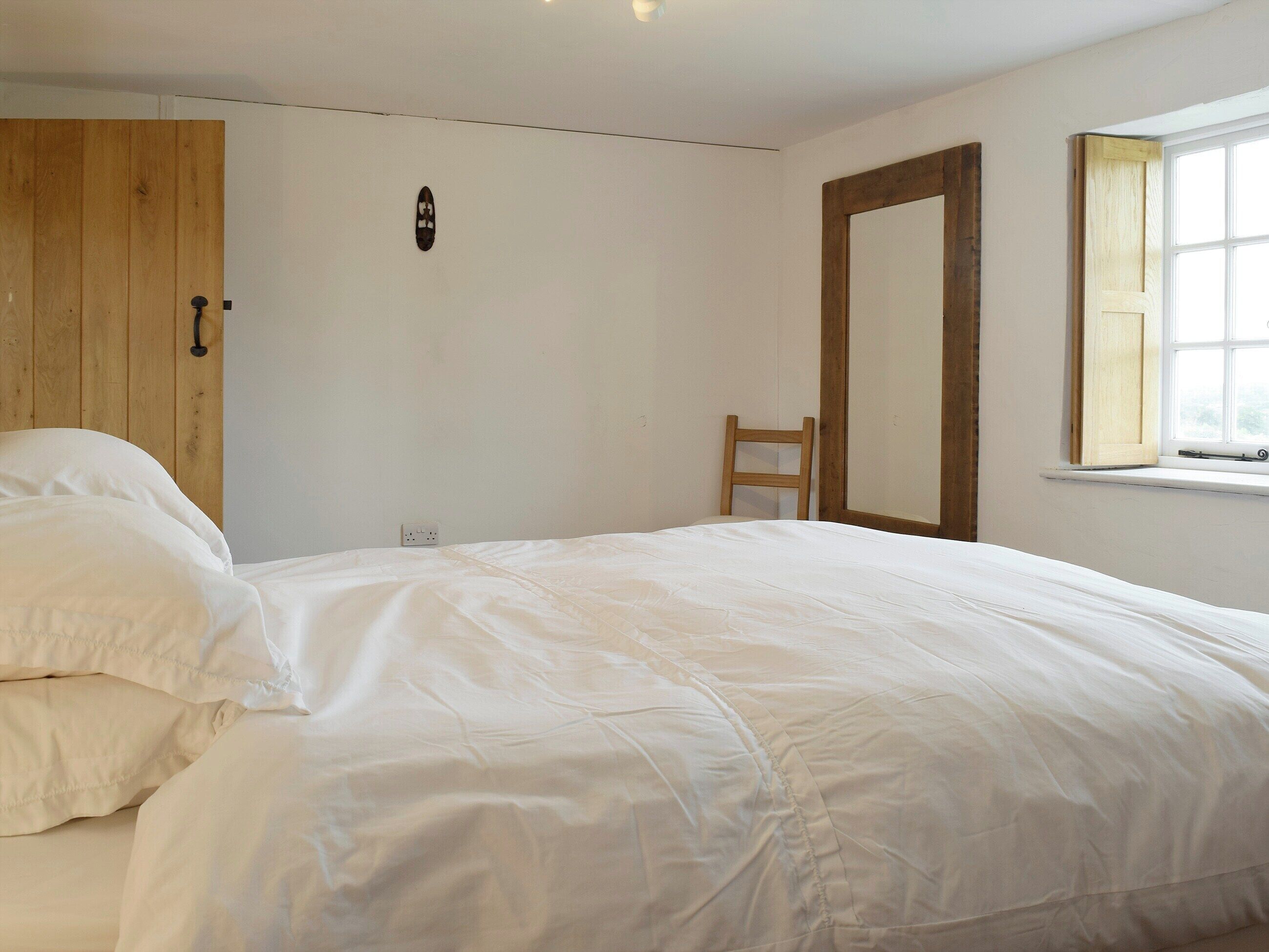 A bedroom with a bed, a wooden wardrobe, a chair, and a window.