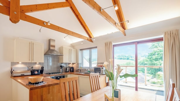 Eine moderne Küche mit Holzbalken, ein Essbereich mit Holztisch und Blick ins Grüne.