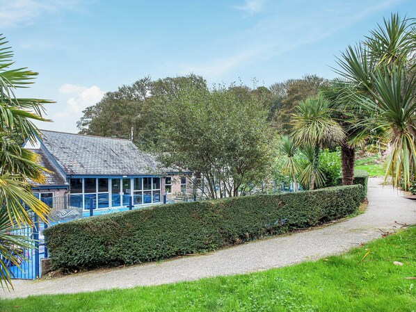 A building with a blue roof and glass windows, surrounded by a well-maintained hedge and palm trees.