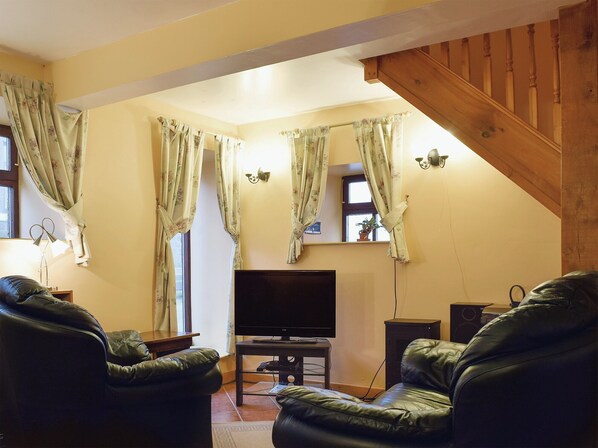 A living room with a TV, leather sofas, and a wooden staircase. - 1 bedroom accommodation in Onecote (Onecote)