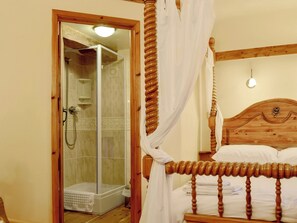 Ein Schlafzimmer mit hölzernem Kopfteil, einem Bett mit weißen Bettwäsche, Holzboden und einer Duschkabine aus Glas.